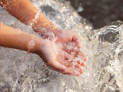 Zwei Kinderhände fangen literweise Wasser auf.